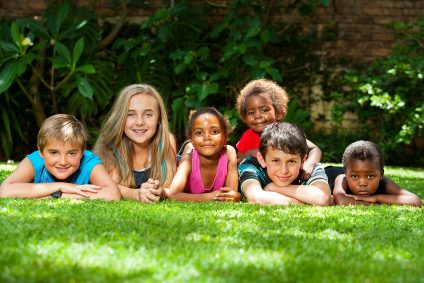 Diversity portrait of children laying together on grass outdoors.